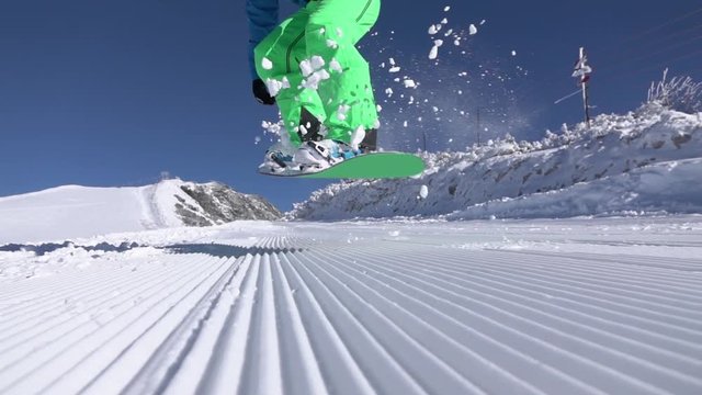 SLOW MOTION: Snowboarder jumping ollie into camera in sunny mountain ski resort