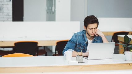 Serious young guy with beard working on laptop