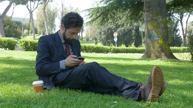 businessman using smartphone and taking a coffee to go on the grass