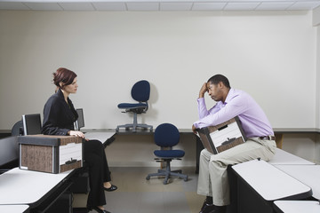 Full length side view of a depressed man with moving box and female manager sitting on desk