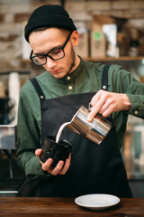 Waiter in black hat fill in a cup of milk