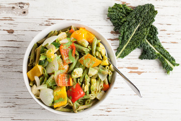 Large white porcelain bowl of pasta and roasted vegetables with a creamy kale sauce above shot