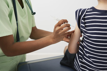 Midsection of a female doctor injecting syringe on boy's arm in the clinic