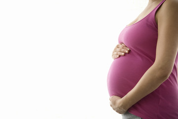 Side view midsection of a pregnant woman with hands holding tummy against white background