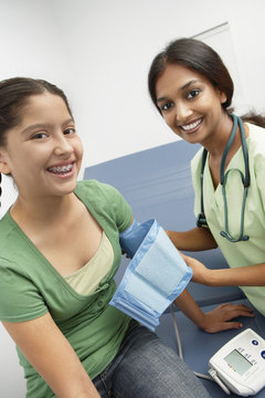 Happy Female Doctor Taking Teenage Girl's Blood Pressure In The Clinic