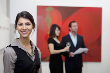 Portrait of smiling young woman in front of a couple in art gallery