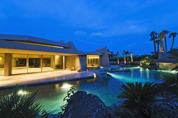 Illuminated house exterior with swimming pool in backyard at dusk