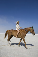 Full length side view of a female riding horse on beach