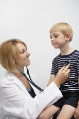 Happy female doctor examining young boy with stethoscope in clinic