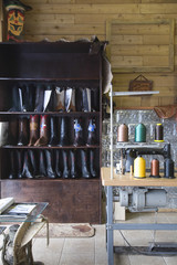 Footwear on shelves by sewing machine at traditional shoemaker workshop - obrazy, fototapety, plakaty