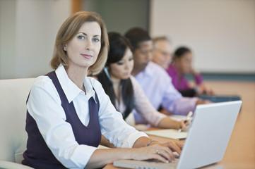 Fototapeta premium Portrait of a confident businesswoman with laptop and multiethnic colleagues in conference room