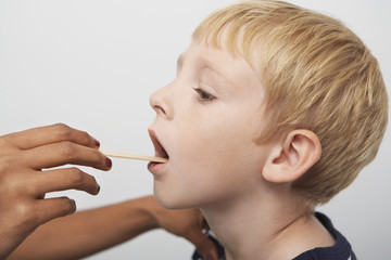 Hands examining patient's throat with tongue depressor in the clinic