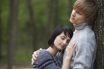 Side view of a young woman laying head on man's chest in woods