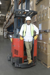 Full length portrait of a man standing with forklift truck in distribution warehouse