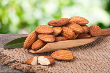 heap of peeled almonds with leaf in a wooden scoop on table blurred garden background