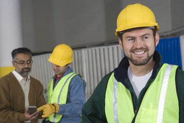 Smiling man in protective wear with colleague in background at factory 