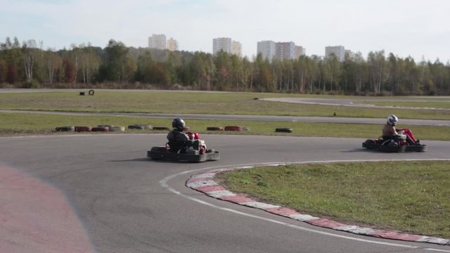 Two drivers in karts are moving very slowly on a ride. Go kart track.