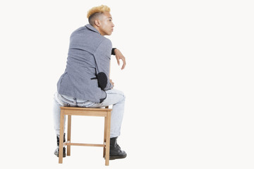 Back view of teenage boy sitting on chair as he looks away over gray background