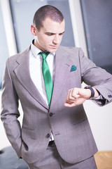 I will be in time. Handsome young man in formalwear looking at his watch while standing.