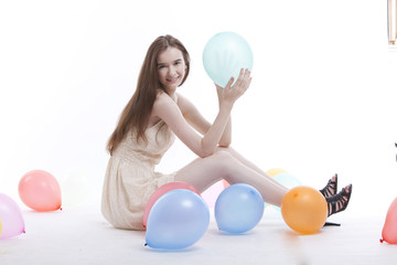 Beautiful young woman in dress on floor with balloons against white background