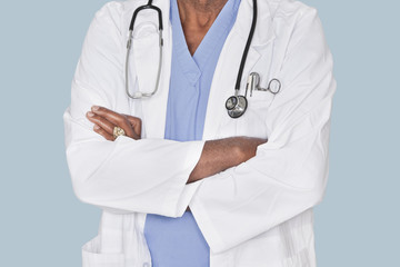 Midsection of a doctor with arms crossed over light blue background