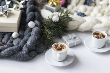 Two cups of coffee and small gift with Christmas decorations on chunky knit blanket