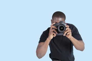 Fototapeta premium African American young man taking photo through digital camera over blue background