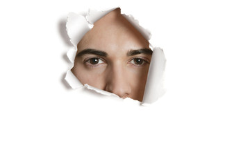 Portrait of a young Caucasian man peeking from ripped paper hole