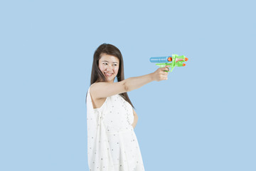 Happy young woman aiming with a toy gun over blue background