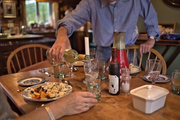 Man in blue shirt  pouring white wine to glass during dinner