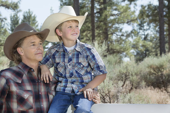 Mature father and son wearing cowboy hats looking away in park