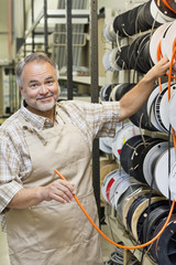 Fototapeta premium Portrait of a happy mature store clerk with electrical wire spool in hardware shop