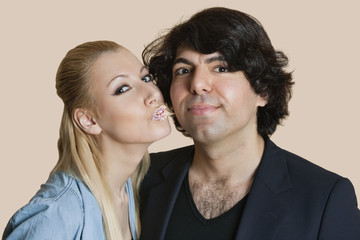 Portrait of a blond woman with sprinkled lips kissing young man over colored background