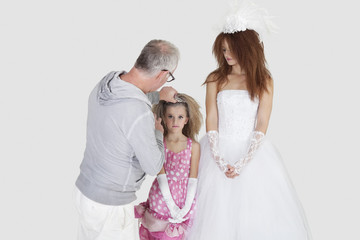 Fototapeta premium Makeup artist with spraying on bridesmaid's hair while bride looking over gray background