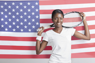Portrait of young woman with tennis racket against American flag