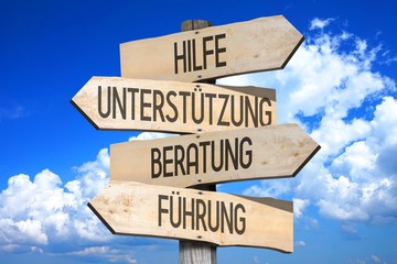 Wooden signpost with four arrows - Hilfe, Unterstutzung, Beratung, Fuhrung - German/ help, support,...