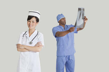 Portrait of happy young nurse with male surgeon examining x-ray report over gray background