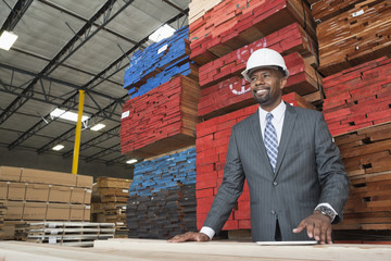 An African American male contractor standing in front of stacked wooden planks
