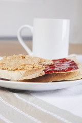 Peanut butter and jam on slices of bread with cup of coffee