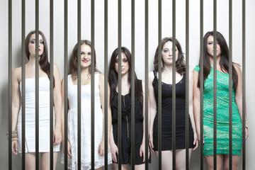 Portrait of five young women standing side by side behinds prison bars