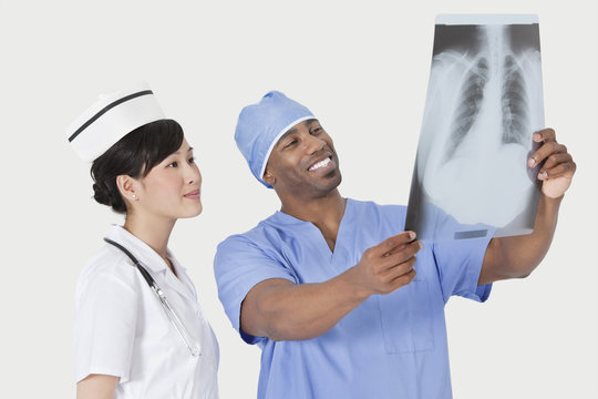 Male surgeon with nurse examining X-ray report over gray background - Powered by Adobe