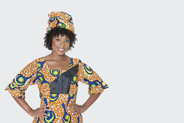 Portrait of young woman in African print attire standing with hands on hips over gray background