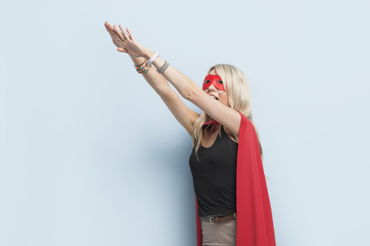 Young woman in superhero outfit pretending to leap in the air against light blue background