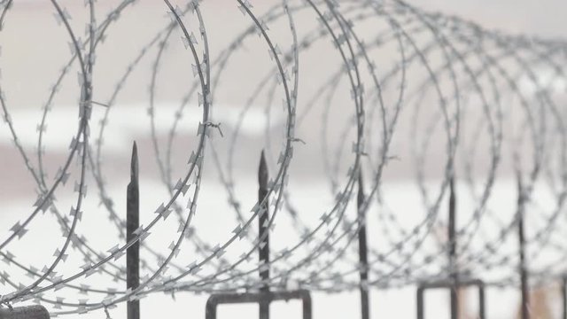 Barbed wire on metal fence with pointed rods. Snowing. Close.