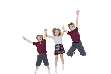 Portrait of happy school children holding hands while jumping over white background