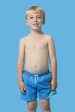 Portrait of a happy young boy in swim trunks over blue background
