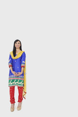 Full length portrait of Indian woman in traditional wear standing over gray background