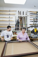 Mature employee measuring picture frame with senior owner in workshop
