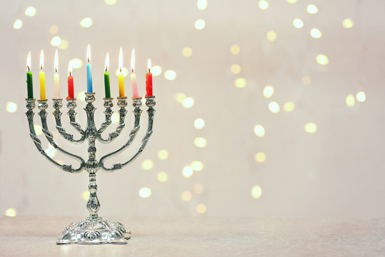 Menorah with colorful candles for Hanukkah on table against defocused lights