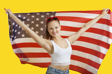 Portrait of happy young woman holding American flag over yellow background